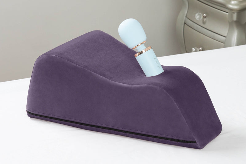 The Liberator Wanda in Plum resting on top of a bed with white sheets. | Kinkly Shop