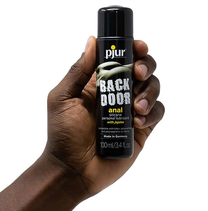 A hand holds a bottle of the Pjur Back Door Anal Silicone-Based in 100ml size. It's a somewhat slender bottle, and it looks like it's shorter than the palm of this person's hand. | Kinkly Shop