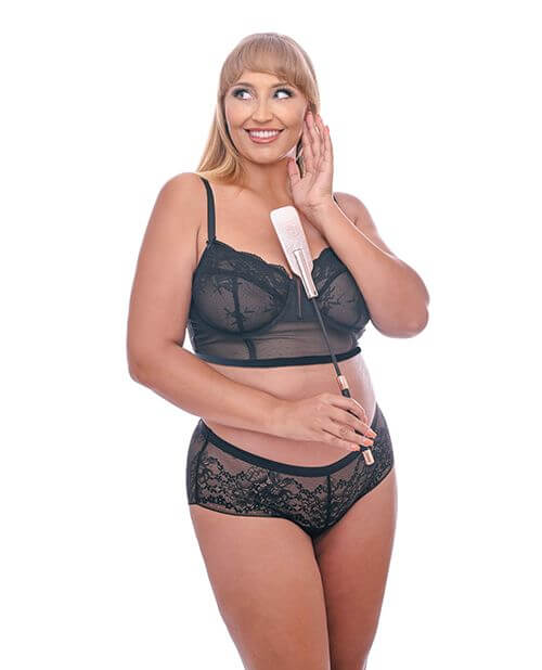 A person in lingerie is smiling and looking off-camera. They're holding the Sportsheets S&M Brat Crop up against their chest. It's slightly longer than their arm and forearm. | Kinkly Shop