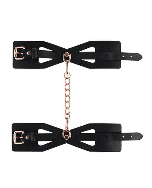 A top-down, lay flat image of the Sportsheets Brat Cuffs and their chain. The two cuffs are laid out flat, and the included chain is shown connecting the two D-rings together. The spot with the D-ring connector is the slimmest part of the cuff with the rest of the cuff at a thicker, wider size. | Kinkly Shop