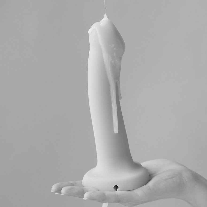 A black and white photo of the Strap-On-Me Silicone Cum Dildo. Cum lube is dripping all down the surface of the dildo as a person holds it in their flat, extended palm. | Kinkly Shop