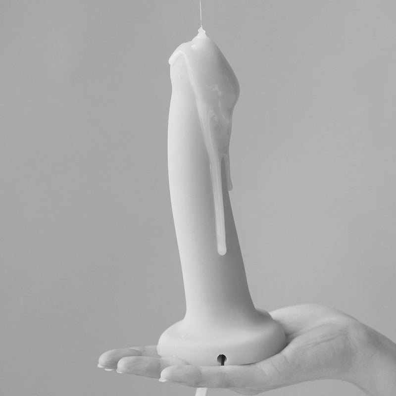 A black and white photo of the Strap-On-Me Silicone Cum Dildo. Cum lube is dripping all down the surface of the dildo as a person holds it in their flat, extended palm. | Kinkly Shop