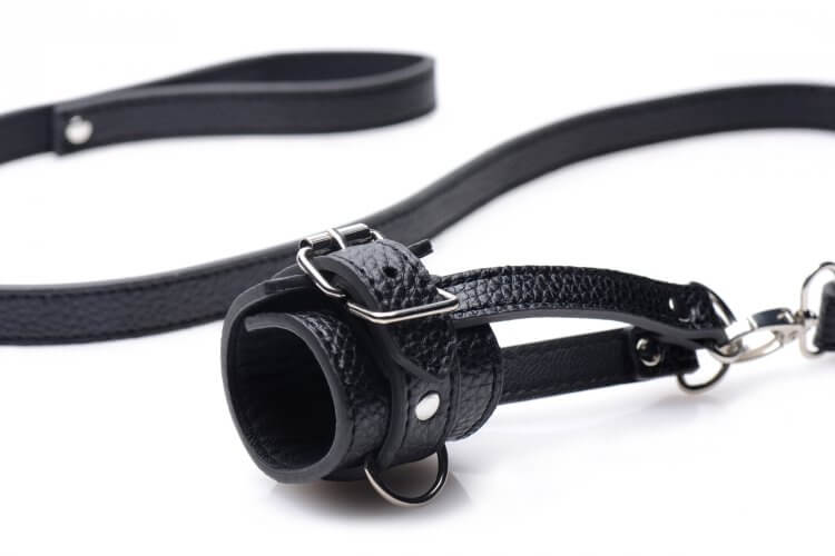 Close-up of the faux leather of the Strict Ball Stretcher with Leash. It uses a standard buckle like most restraints for a familiar experience. The Ball Stretcher also has D-rings located on the ball stretcher itself in addition to the two hanging straps that feature D-rings. | Kinkly Shop