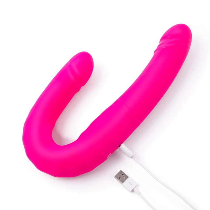 The Together Toy Duo Together, bent into a U-shape, plugged into the charger. The charging point is towards the centerpoint of the dildo. | Kinkly Shop