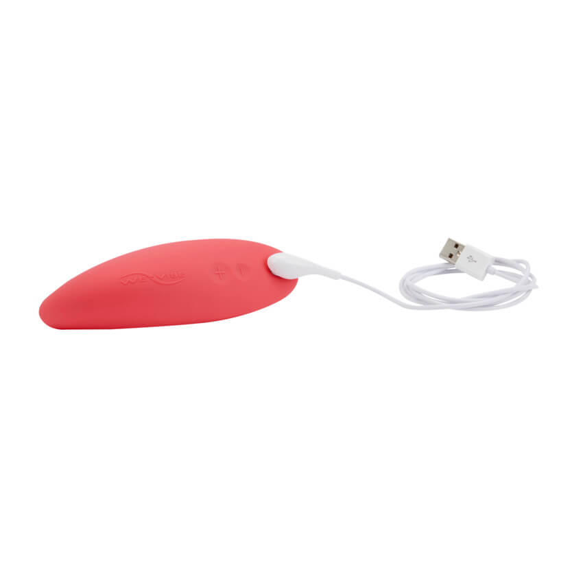 The We-Vibe Melt lays on a plain white surface with the charging cable attached. The cable has a magnetic connection point with a male USB connector on the opposite end. | Kinkly Shop