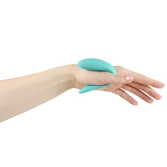 The We-Vibe Sync Lite in Aqua squeezed around the thumb of someone's palm. This showcases how the U-shaped design can fit inside and outside of the body at the same time. | Kinkly Shop
