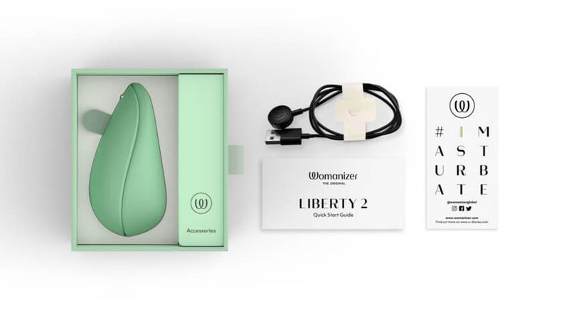 The Womanizer Liberty 2 in its packaging next to everything it comes with. There's the charging cable, a sticker, and the Quick Start guide. | Kinkly Shop