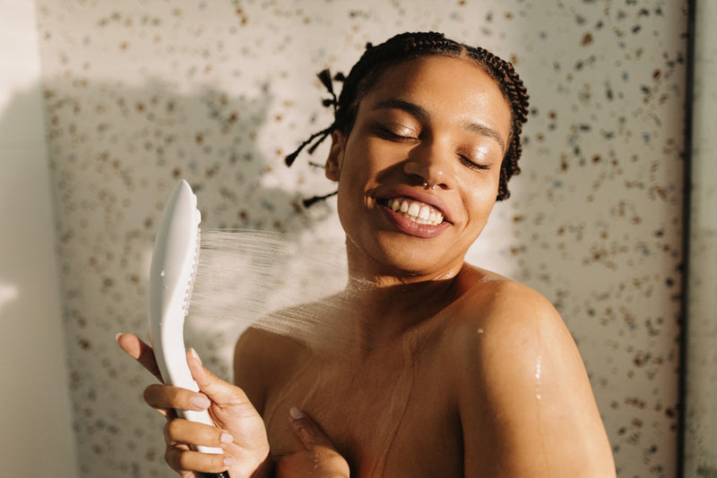 A person holds the Womanizer Wave shower head up against their neck as it pours water onto them. They're smiling. | Kinkly Shop