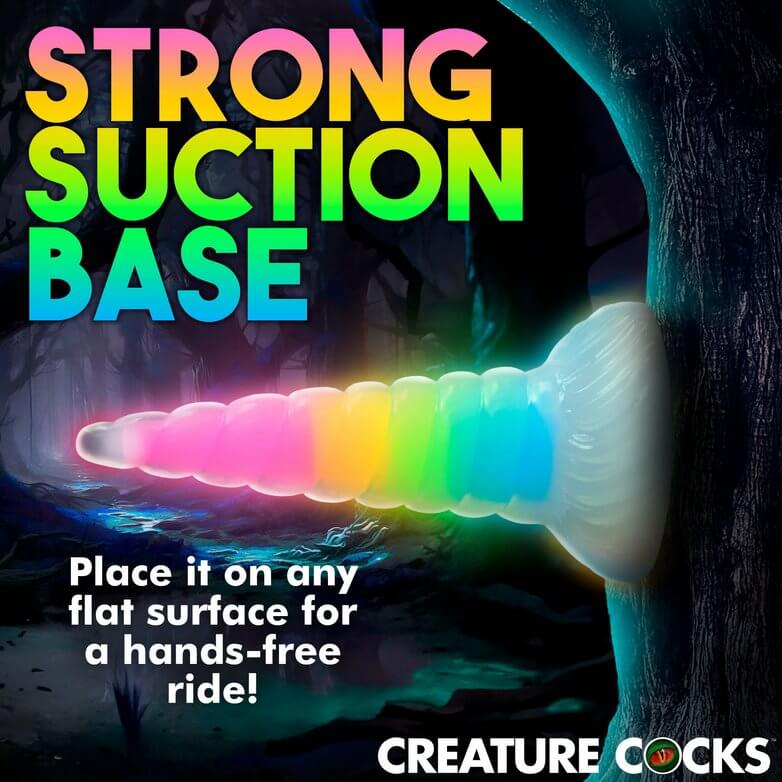 The Creature Cocks Uni Glow dildo shown adhered up to a tree. Text on the image reads "Strong suction base. Place it on any flat surface for a hands-free ride." | Kinkly Shop