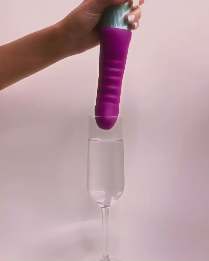 GIF shows a hand holding the tip of the FemmeFunn Cadenza in a glass of water. As the FemmeFunn Cadenza's intensity level is turned up, the water splashes out of the glass and all over the place. | Kinkly Shop