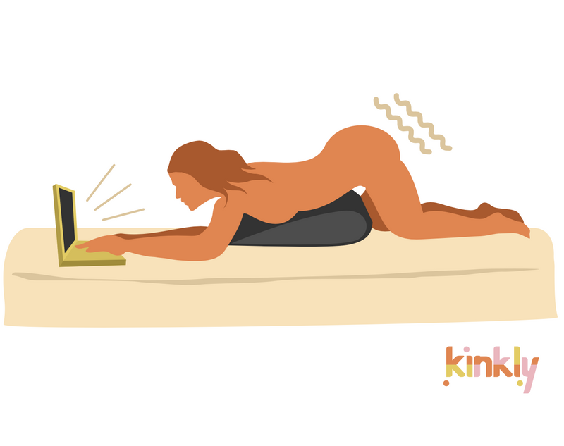 Browse and Buzz sex position. A solo person is laying down on their stomach. A triangular piece of sex furniture is propped underneath them, holding a vibrator between their thighs. The person uses their laptop with both hands as the sex furniture is holding the vibrator in place for them.