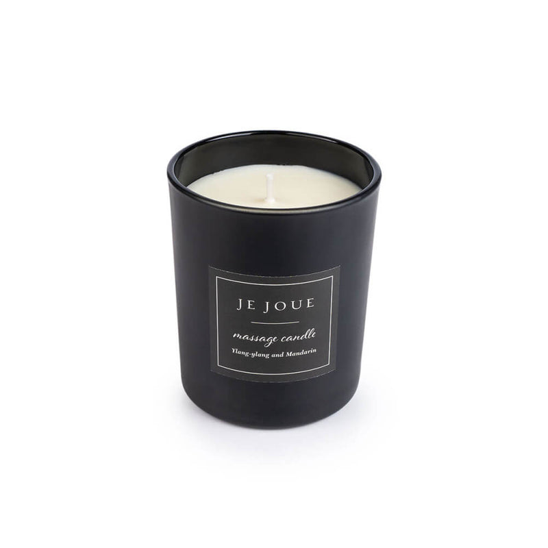 The massage candle included within the Je Joue Naughty Collection set. The candle is in a large, glass candle jar that's very sultry-looking in black. A sticker on the front of the candle reads "Je Joue Massage Candle". | Kinkly Shop