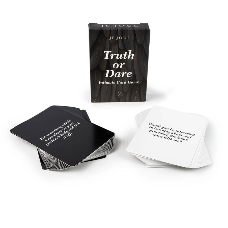 The box for the Je Joue Naughty Collection Truth or Dare set is sitting upright in the background while two stacks of cards (one Truth, one Dare) sit out in the foreground. The Dare card that is shown reads "Put something edible somewhere on your partner's body and lick it off." and the Truth card reads "Would you be interested in learning about and practicing the Kama Sutra with me?" | Kinkly Shop