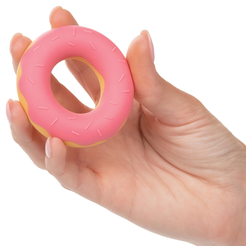 A hand holds the Naughty Bits Dickin' Donuts between all of the fingers. It's a relatively thick cock ring compared to most cock rings. It looks like the open center is about the same as most standard, edible donuts - but the Naughty Bits Dickin' Donuts ring does not have as thick of a "donut" as most edible donuts would be. | Kinkly Shop