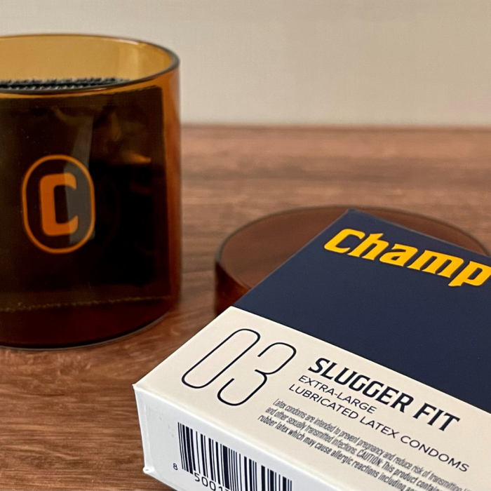 The box of condoms sits out on top of a wooden countertop. There's a Champ-branded candle in the background. | Kinkly Shop