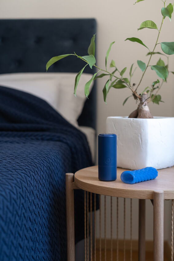 The Arcwave Ghost sitting next to the bed on the bedside table. It looks slightly taller - but much thinner - than a soda can. The stroker lays out flat on the table next to the case. It looks very stretchy and squishy as it is in more of an oval shape due to laying flat with gravity. | Kinkly Shop