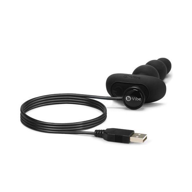 The b-Vibe Triplet Anal Beads laying flat while the magnetic charging cable is attached to its base. The other end of the charging cable is shown with its USB connector. | Kinkly Shop