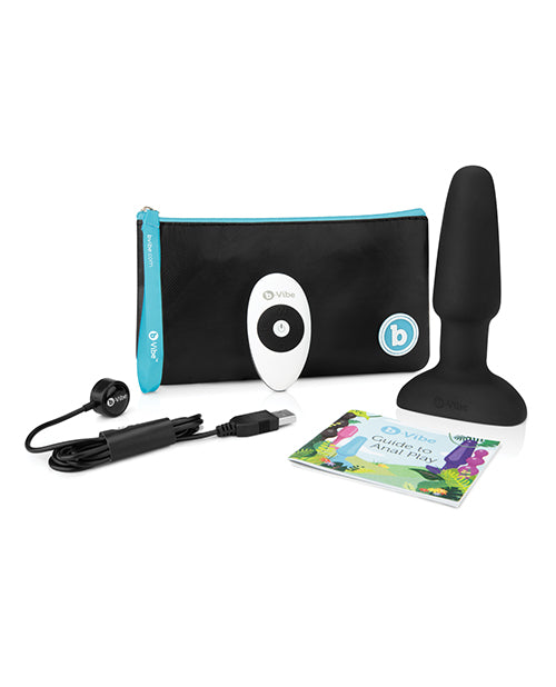 The b-Vibe Rimming Plug 2 with everything that it comes with. This includes the plug itself, the remote, the Guide to Anal Play, the charging cable, and a branded zippered pouch to store it all in. | Kinkly Shop
