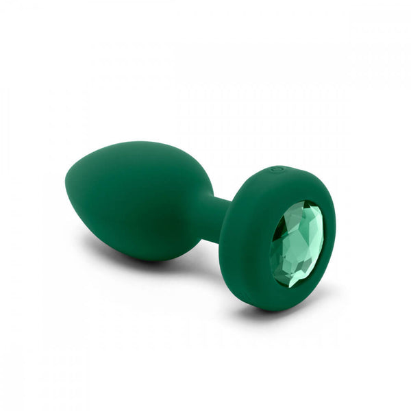 An angled shot of the b-Vibe Vibrating Jewel Remote Control Butt Plug in Emerald. It shows the very tapered, torpedo-like design of the insertable portion with the round base that's inset with the gem. | Kinkly Shop