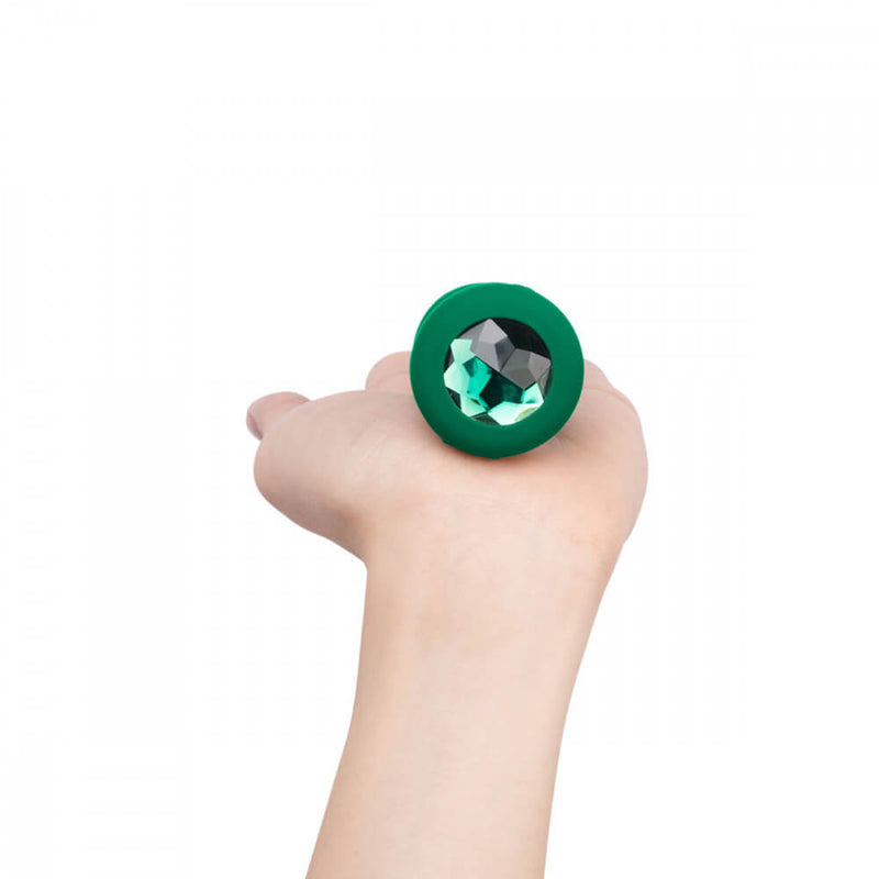 A hand holds the b-Vibe Vibrating Jewel Remote Control Butt Plug at an angle where you can only see the gem at the base. This shows how small the base's footprint is. | Kinkly Shop