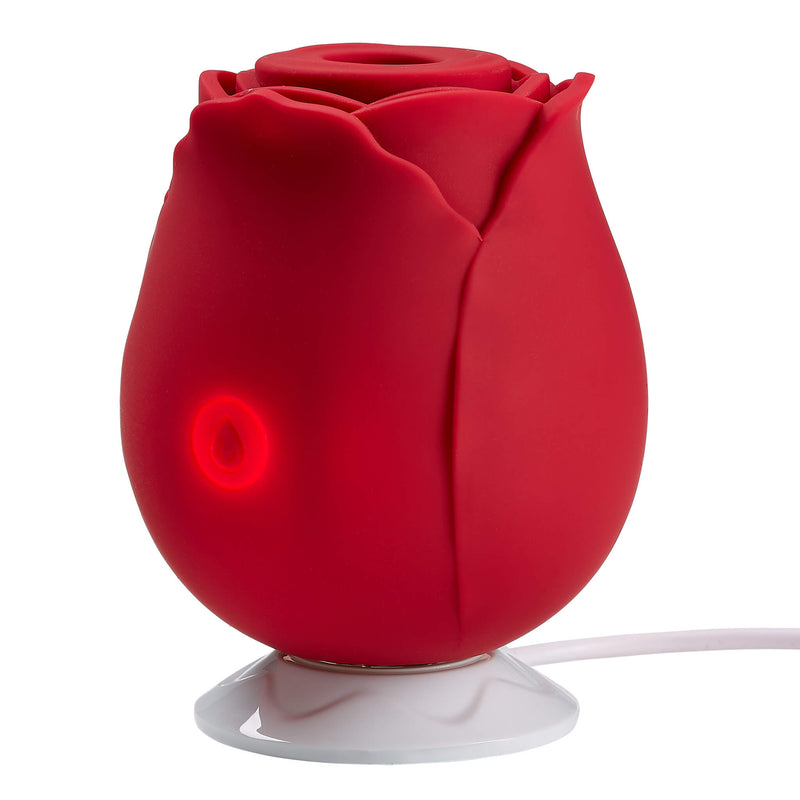 The Cloud 9 Rose Suction Stimulator sits on top of its charging base. The charging base's cord, which leads off-picture, must be plugged in because the vibrator's control button is backlit to mean that it's charging. The charging base holds the vibrator upright while charging. | Kinkly Shop