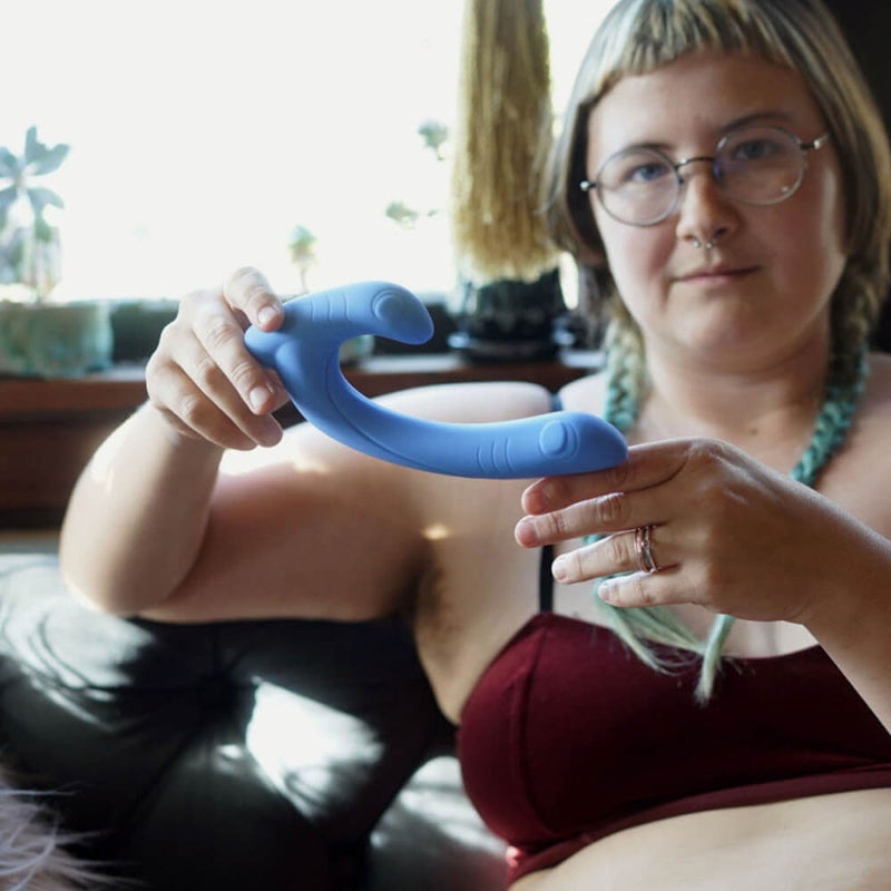 A person holds the Cute Little Fuckers Jix up. The camera is focused on the vibe. In the background, the person looks into the camera with two braided pigtails while sitting on a couch. | Kinkly Shop