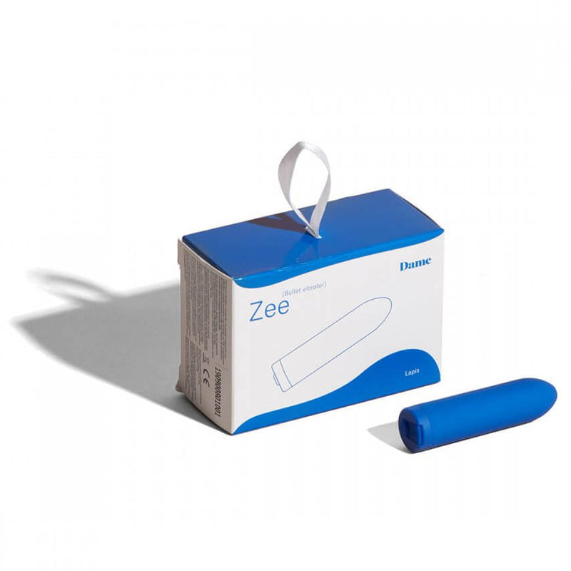 The Dame Zee micro bullet vibrator rests in front of the packaging for the Dame Zee micro bullet vibrator. | Kinkly Shop