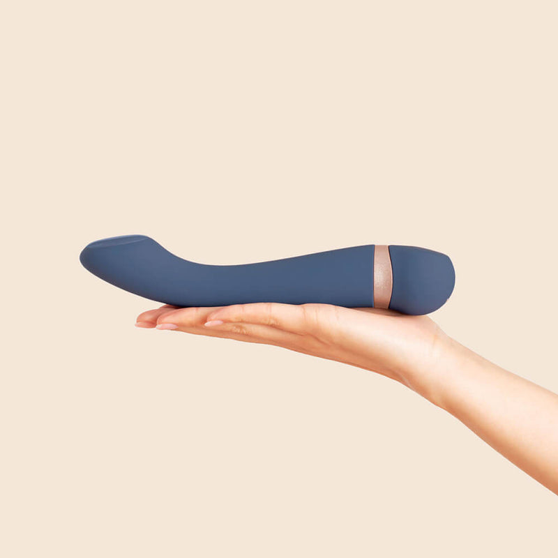 A person lays their palm out flat, and the Deia Hot & Cold Temperature Play Vibrator rests on top of their palm. This displays the g-spot curve of the tip that is clearly prounced from the rest of the straight shaft. The vibrator is longer than the person's hand and extends past their fingers. | Kinkly Shop