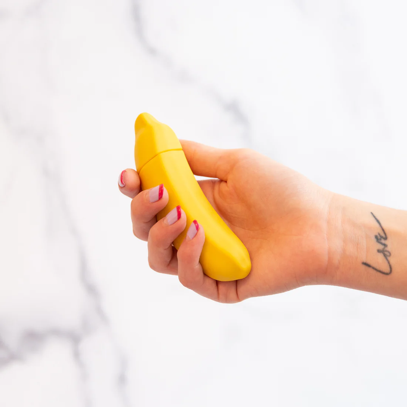 A hand holds the Emojibator Banana. The banana is shorter in length than a full-size banana you'd get at the grocery store, but it has about the same diameter as a standard banana. | Kinkly Shop