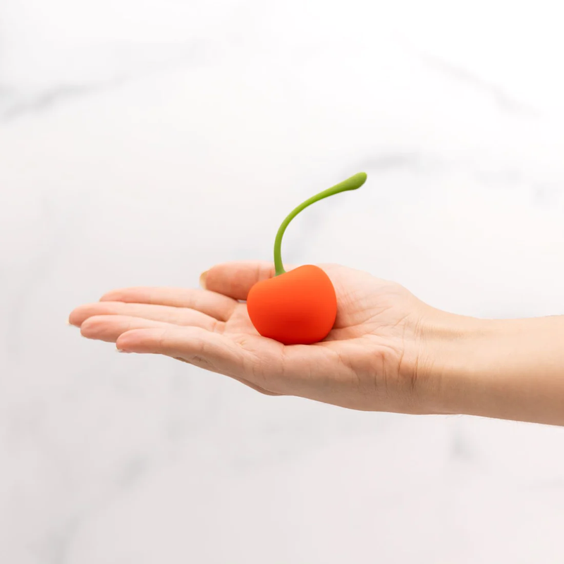 A hand is held out flat. The Emojibator Cherry is resting in the middle of the palm of the hand. It is smaller than the palm, but it looks closer to the size of a small tomato than a regular-sized cherry. | Kinkly Shop