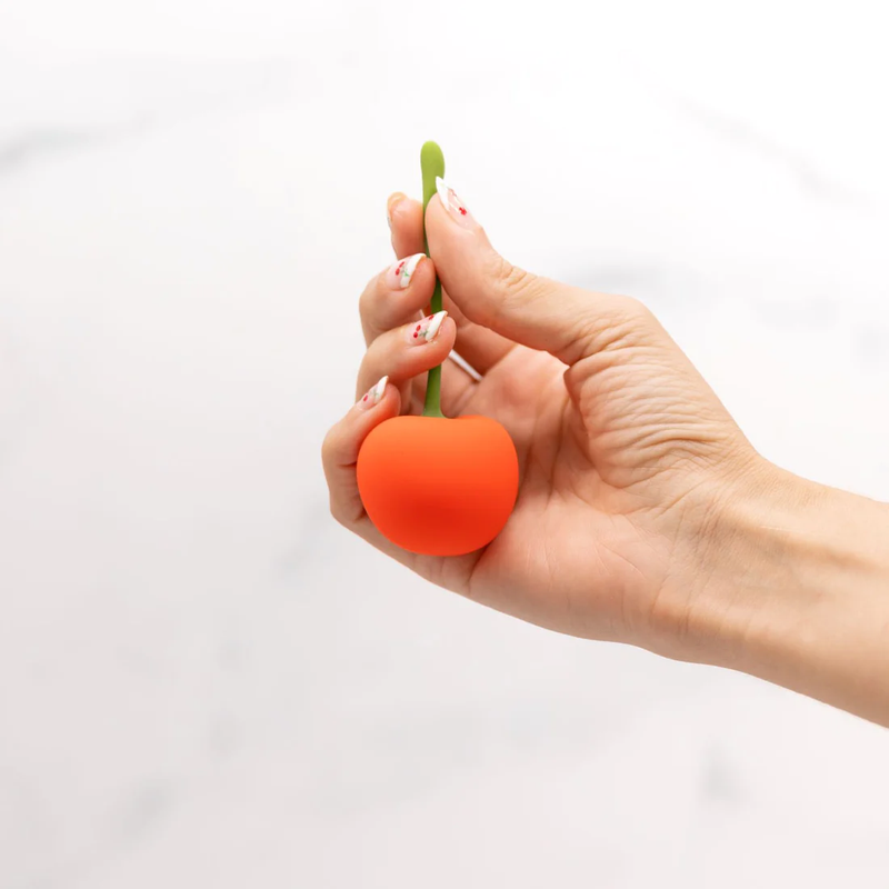 A hand holds the Emojibator Cherry by its stem. The stem looks flexible, and holding it by the stem appears to support the weight of the vibrator at the end of the stem. | Kinkly Shop
