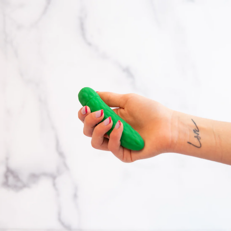 A hand holds the Emojibator Pickle. Their fingers appear to be able to curl around the thickness of the Emojibator Pickle pretty well. The Pickle is shorter than their palm to their fingertips, but not by a lot. | Kinkly Shop