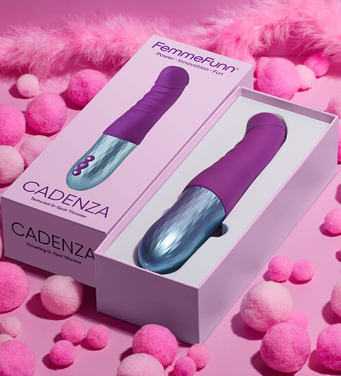 The FemmeFunn Cadenza laying out on a pink, decorated background. The toy is resting inside of the formed tray in theFemmeFunn Cadenza box. | Kinkly Shop
