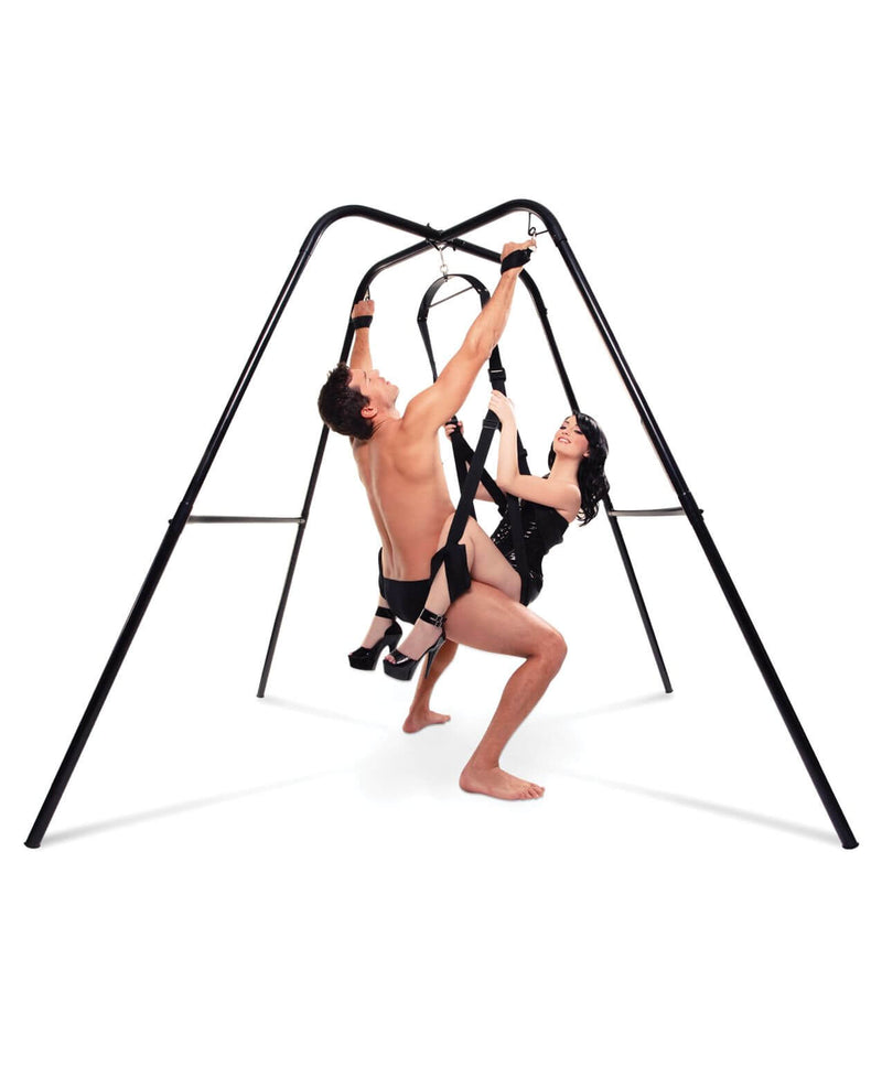 Two people are using a sex swing that's hanging from the Fetish Fantasy Series Sex Swing Stand. The person sitting on top of the sex swing also has their hands bound up above their head using the bondage loops built into the frame. | Kinkly Shop