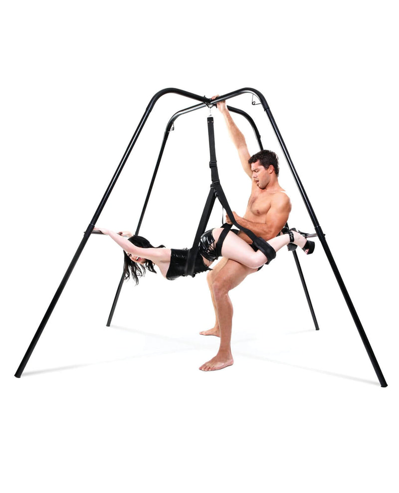 Two people are enjoying the Fetish Fantasy Series Sex Swing Stand with a swing hung from it. The person laying in the sex swing is using their wrists on the support beam on one side. The standing, penetrating partner is gripping the top of the frame for additional support to hold their sex position as well. | Kinkly Shop