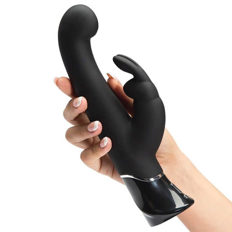 A hand holding the Fifty Shades of Grey Greedy Girl Rabbit Vibrator. It shows the size of this rabbit vibrator which is noticeably longer than a hand. It has an accordion-style area on the middle of the shaft that helps facilitate the thrusting of the tip. | Kinkly Shop