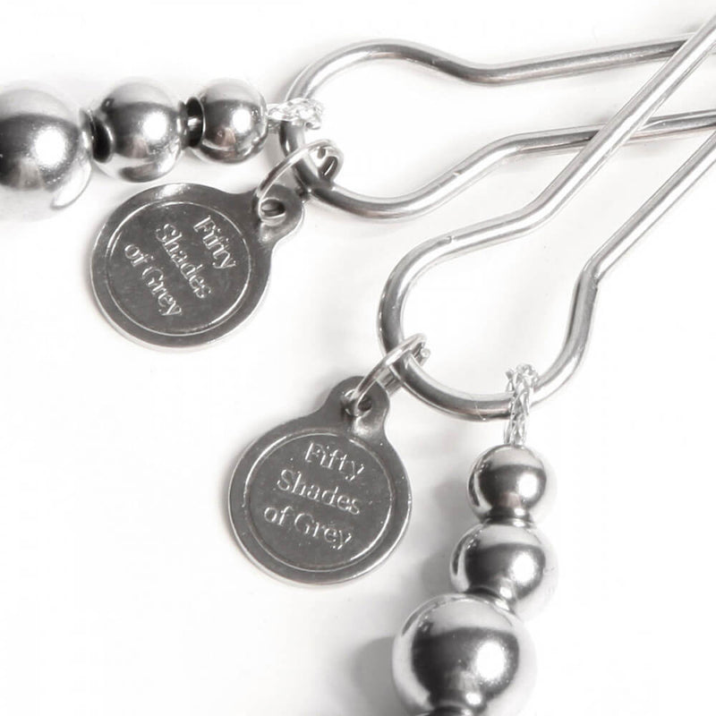 Close-up of the Fifty Shades of Grey Pinch Nipple Clamps charms on the base of each nipple clamp. They have the word "Fifty Shades of Grey" etched into the metal plaque. These charms are held on by a loop of metal that can easily be removed if the charms aren't desired. | Kinkly Shop