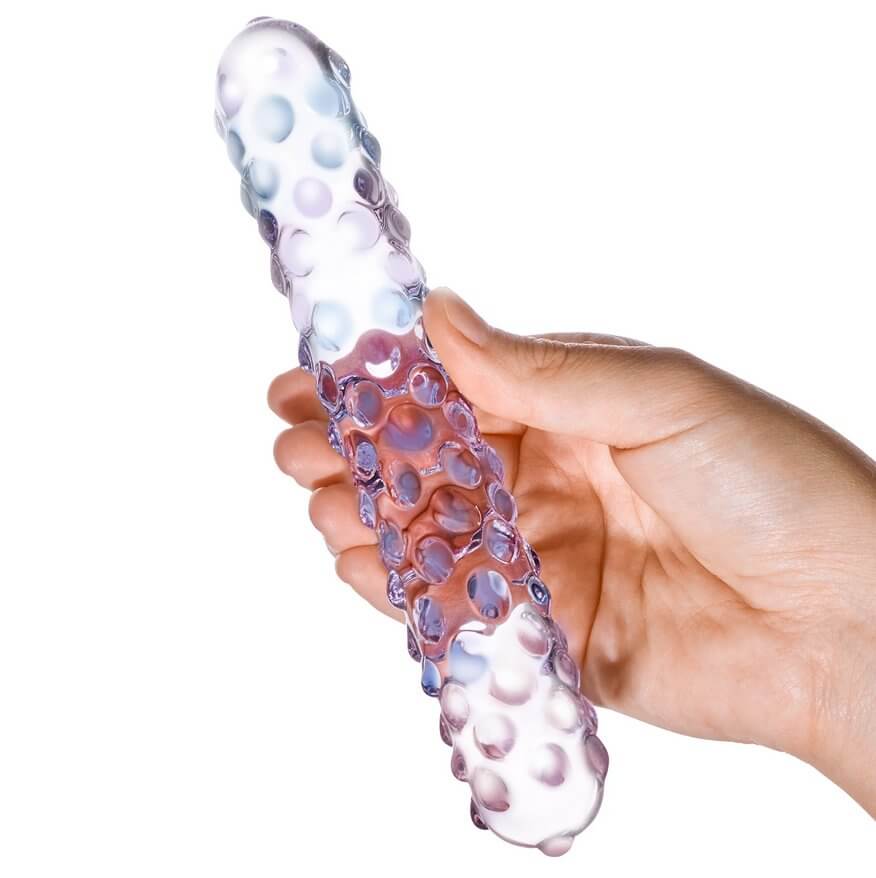 A person holds the Purple Rose Nubby dildo in their hand. This showcases the see-through design of the dildo as the hand can be seen through the shaft of the dildo. | Kinkly Shop