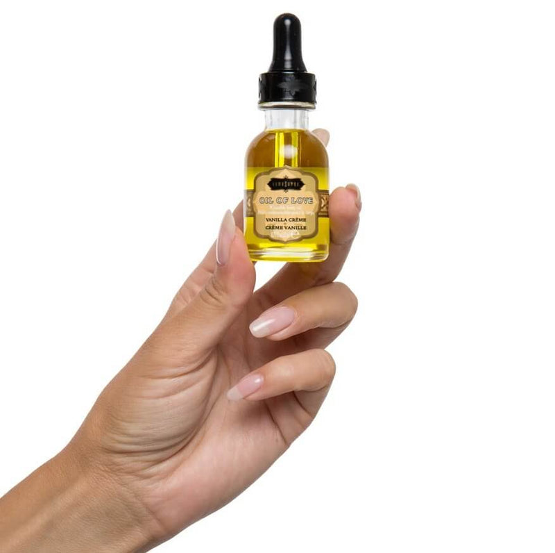 A hand holds the Oil of Love bottle from the Kama Sutra Feel Me Kit. It is about the length of a finger, and it includes a cap that has a dropper for easy application. | Kinkly Shop