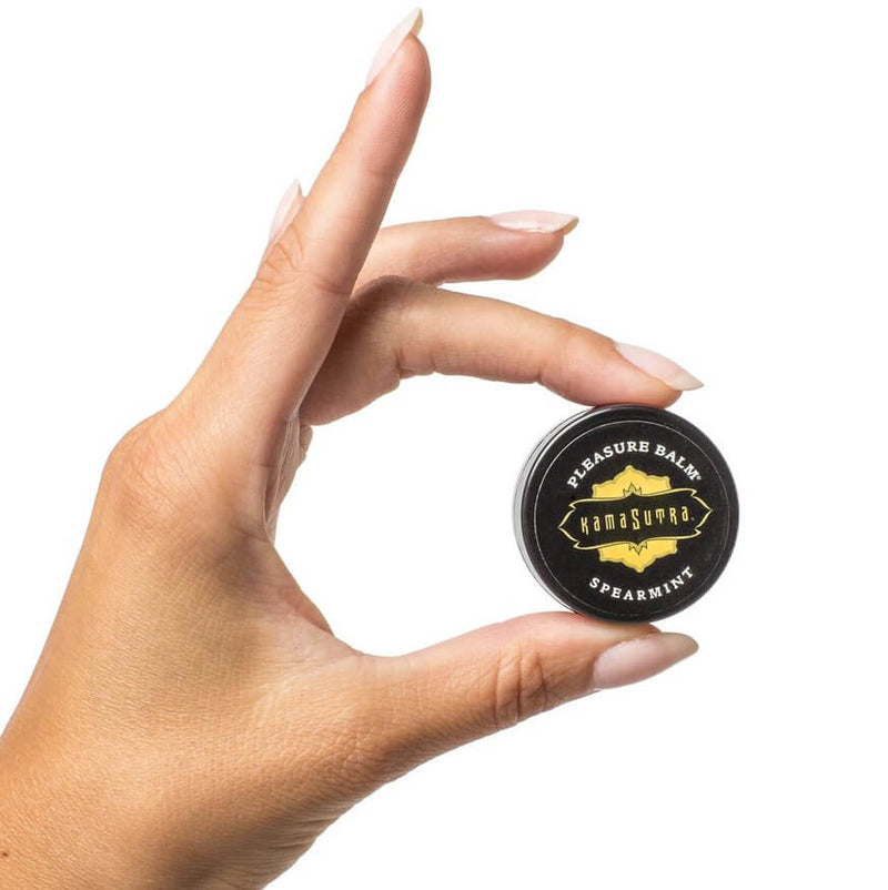 Two fingers pinch a balm-sized tube of the Pleasure Palm included in the Kama Sutra Feel Me Kit. It looks like a standard lip balm tin. | Kinkly Shop