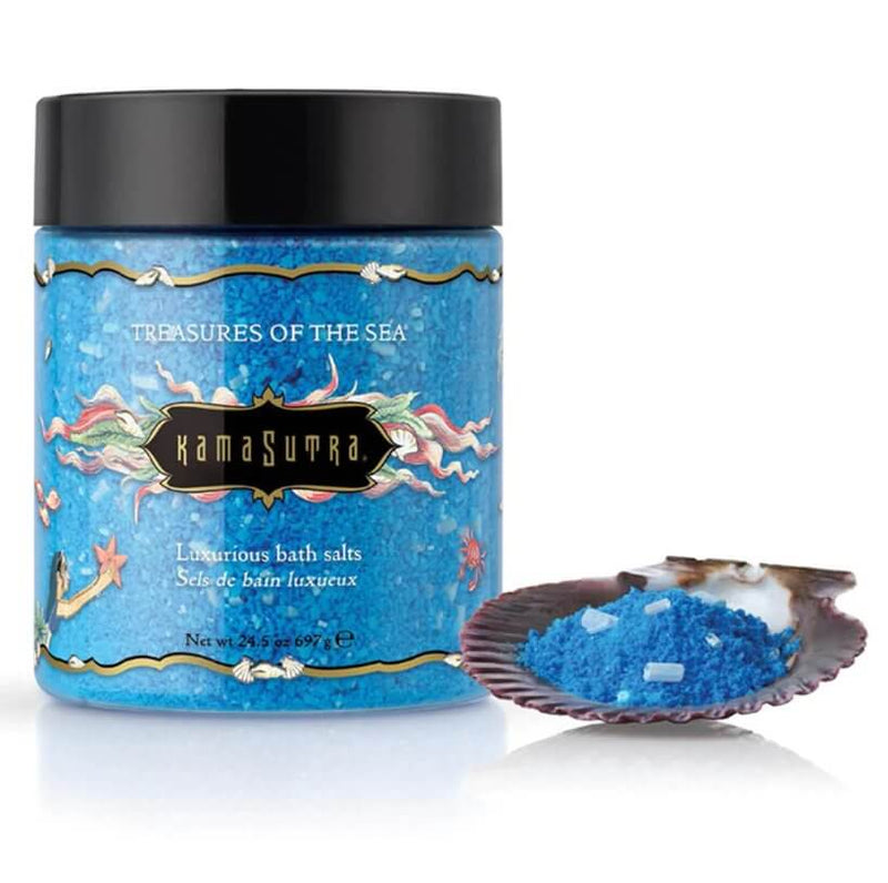 Kama Sutra Treasures of the Sea Bath Salts in front of a white background. A small brown shell is shown in the foreground that is holding some of the blue balt salts, ready to pour. | Kinkly Shop