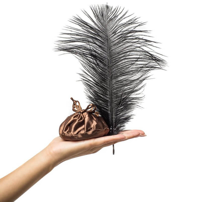 A person holds the Honey Dust from the Kama Sutra Trust Me Erotic Playset with a flat palm. The Honey Dust is packaged in a drawstring bag, and the included feather is large and fluffy. It looks like a very sensual tool to apply the dust to the skin. | Kinkly Shop