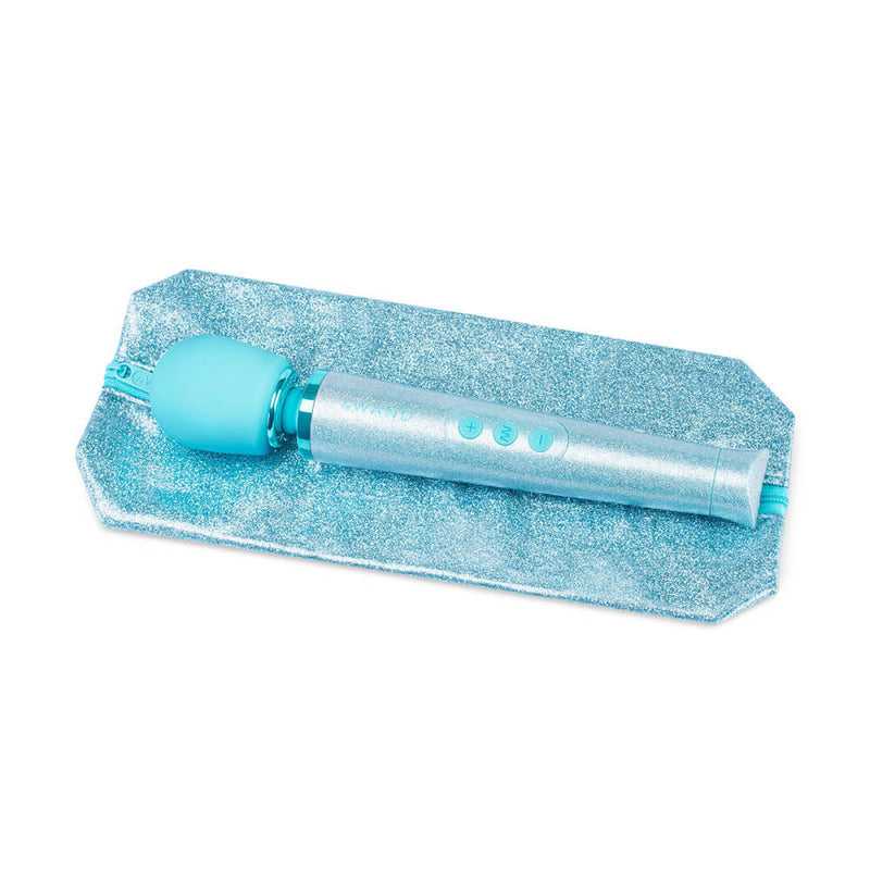The Le Wand All that Glimmers Wand Massager laying out on top of its matching, zippered storage bag. The bag is extremely glittery and sparkly just like the wand massager is. It looks sealed with a plastic to keep the glitter from escaping. | Kinkly Shop