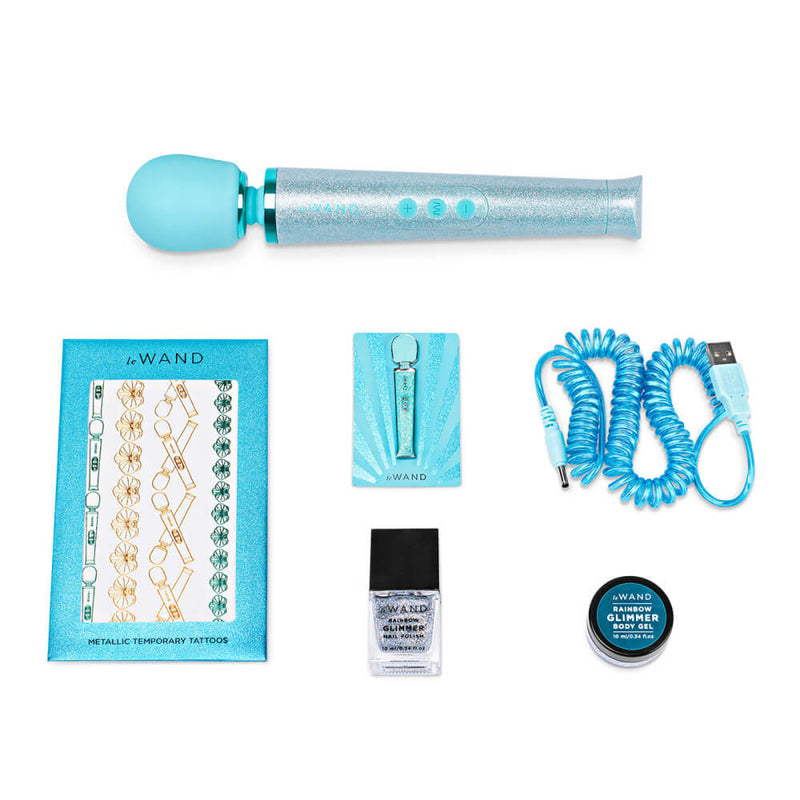 The Blue Le Wand All That Glimmers Wand Massager laid out next to everything that comes with the petite wand massager. That includes the color-coded charging cable, a glittery body gel, a matching enamel pin, a glittery nail polish, and a set of color-matching metallic temporary tattoos. | Kinkly Shop