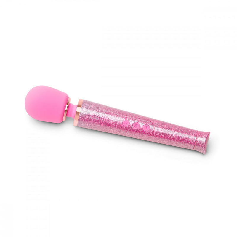 The Pink Le Wand All That Glimmers Wand Massager laying out on a flat surface. The wand's handle is extremely sparkly and glittery. The head of the petite wand massager is in a color-matching silicone. The three buttons on the handle also match the silicone look of the head. | Kinkly Shop