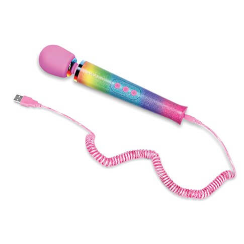 The Le Wand Rainbow Ombre Petite Wand Massager laid out against a white background, plugged into its sparkly, pink charging cable. The other end of the charging cable is just laying out, showcasing the USB-end of the cable. It also showcases the wrapped cord design of the charging cable that looks like the old telephone cords. | Kinkly Shop