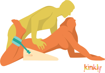 Illustrated sex position shows the receiving partner laying on their stomach with their hips propped in the air. The receiving partner's ankles are bound in cuffs that are attached to the Liberator Black Label Wedge. The penetrating partner climbs on top of them from behind for sex. | Kinkly Shop