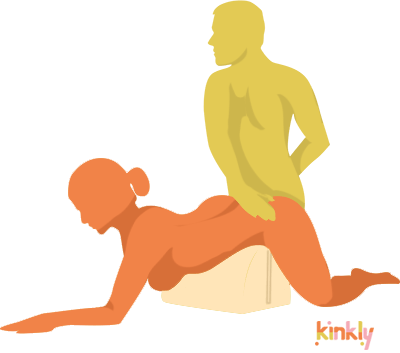 An illustrated sex position that shows the receptive partner leaning over the Liberator BonBon Sex Toy Mount , doggy style, with the BonBon Liberator supporting their hips. The penetrating partner is kneeling behind them to enter them. | Kinkly Shop