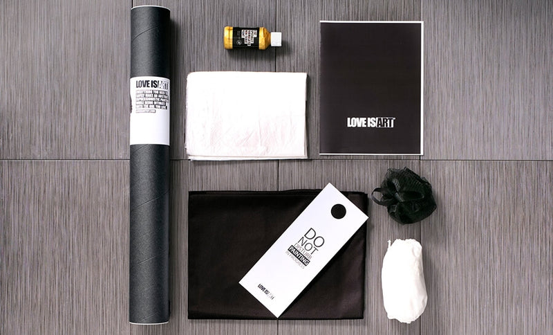All of the items that are included within the Liberator Love is Art Romantic Canvas and Paint Kit. The image shows the tube that canvas comes in, the tarp that protects your floor, the canvas itself, the mesh sponge, the disposable booties, the instructions, and the non-toxic paint (of your kit's color choice.) | Kinkly Shop