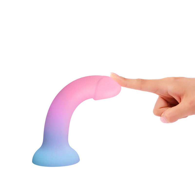 The Love to Love DilDolls is suctioned to a white surface. One finger applies pressure to the tip of the dildo to showcase how flexible the material is and how much it can bend. | Kinkly Shop